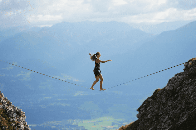photo d’une personne qui tente de garder l’équilibre sur une corde accrochée entre deux montagnes